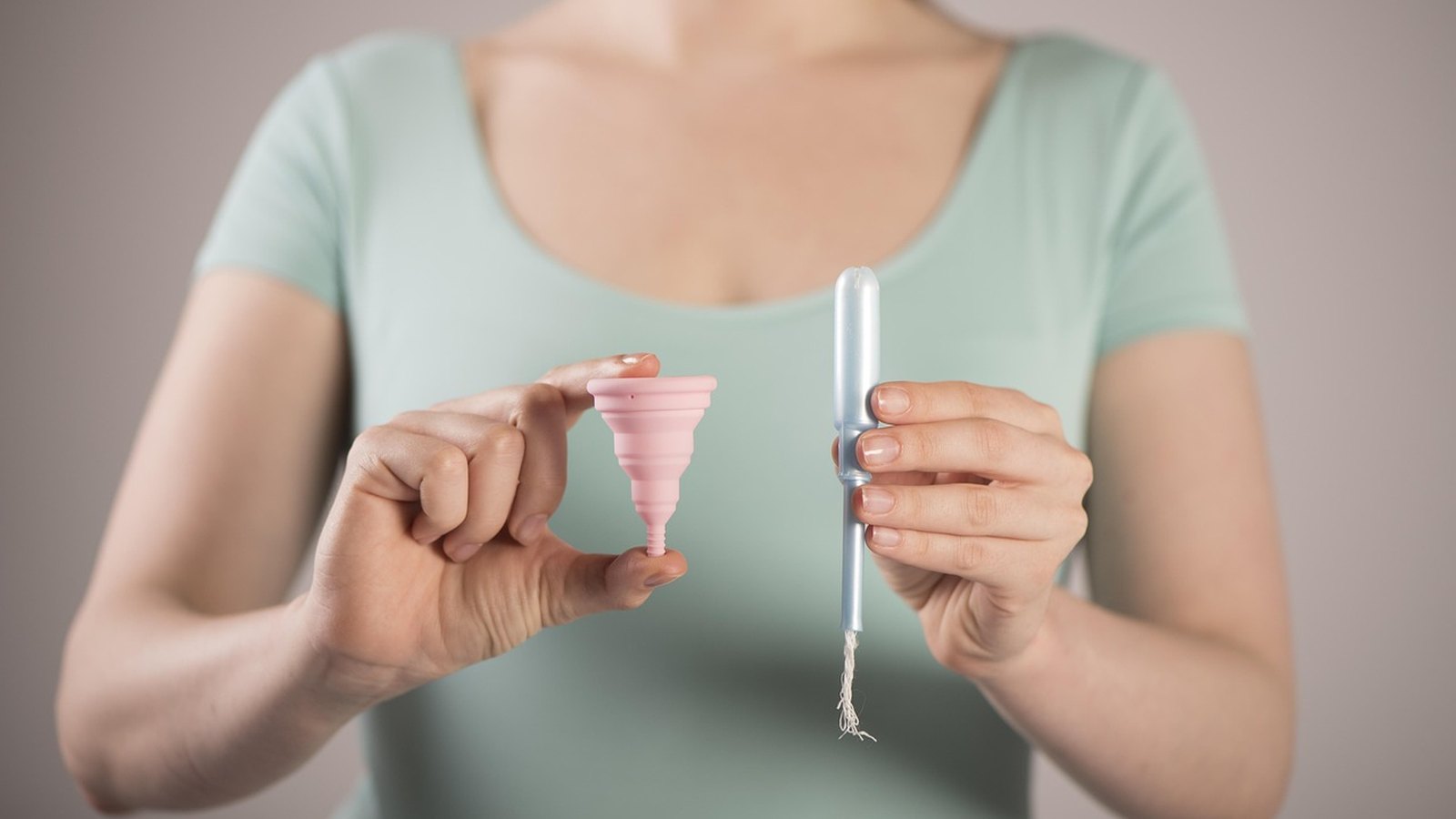 Žena drží v jednej ruke ružový menštruačný kalíšok a v druhej tampón