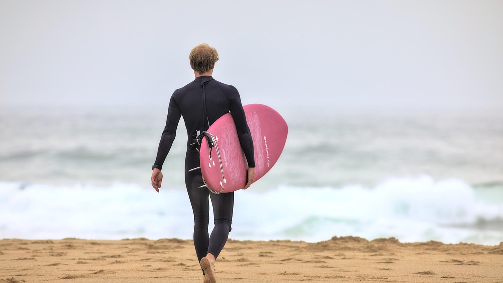 Surfer v neoprénovom obleku kráča s doskou k moru