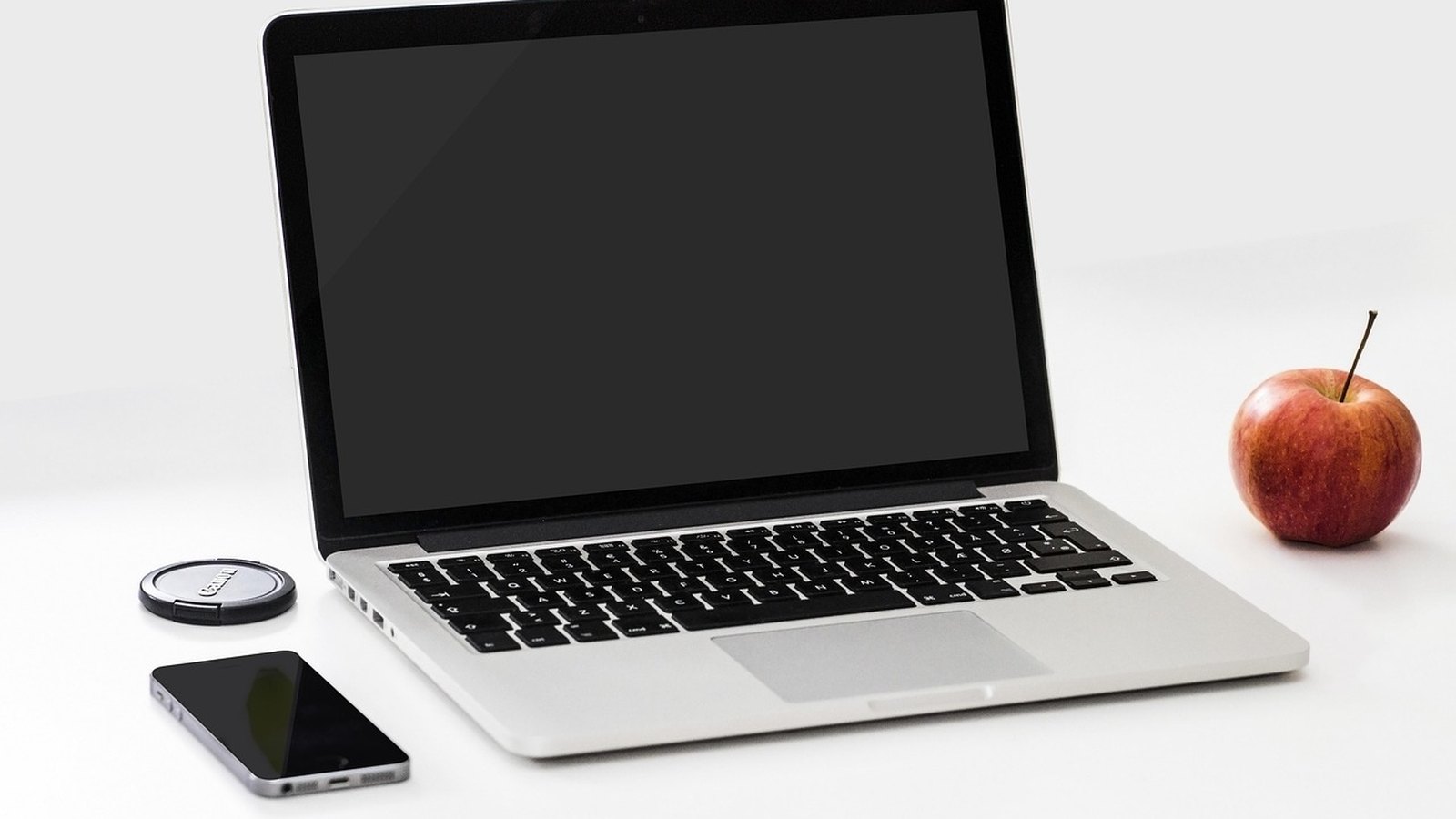 Otvorený strieborný notebook vedľa mobilu a jablka