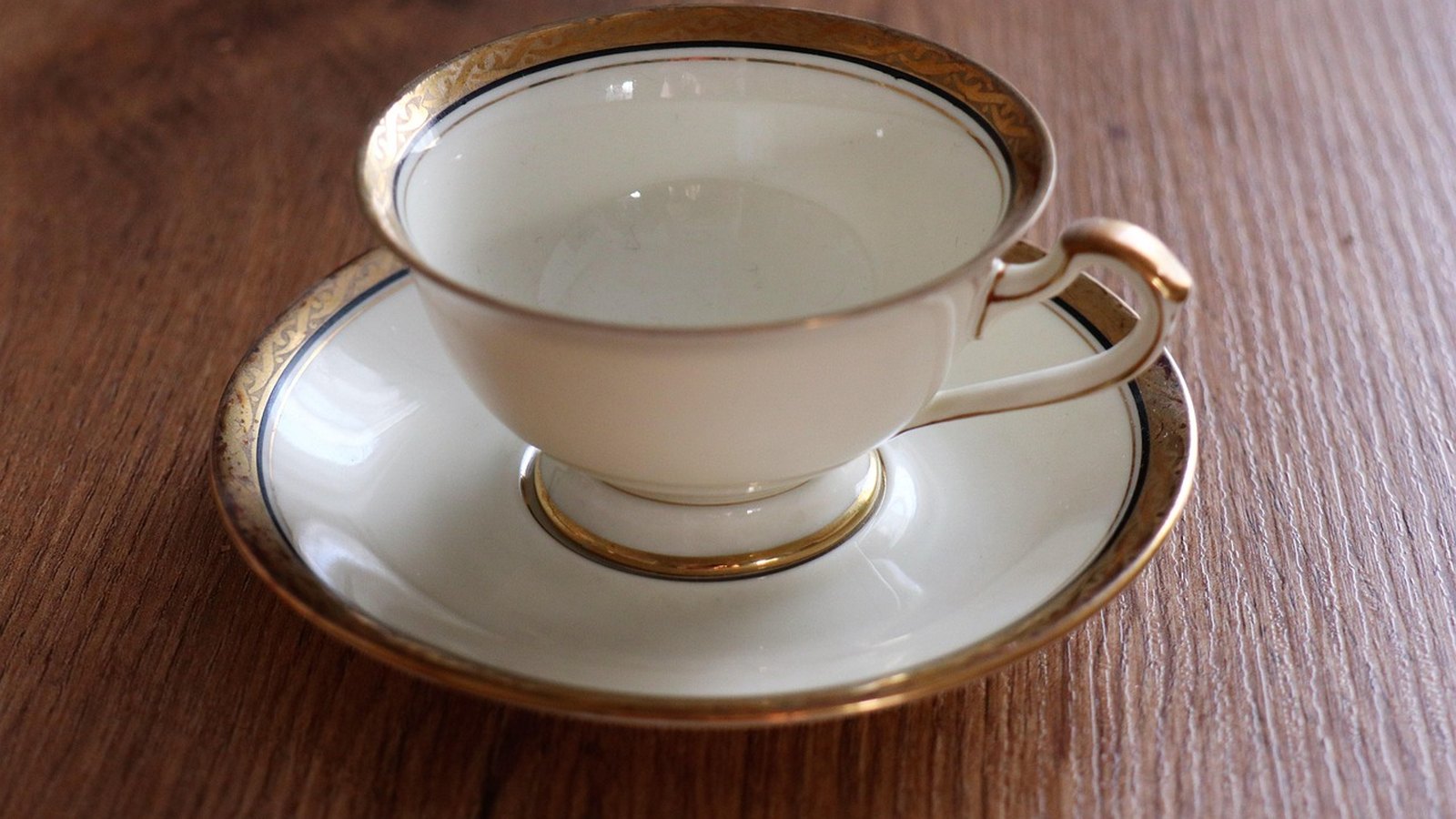 Biela porcelánová šálka so zlatým okrajom na tanieriku