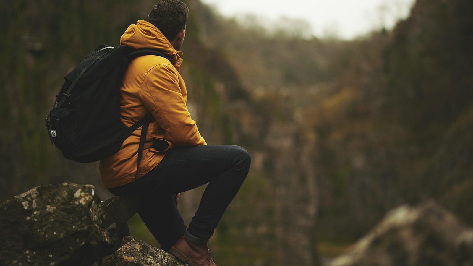 Turista v žltej bunde s batohom sedí na skale